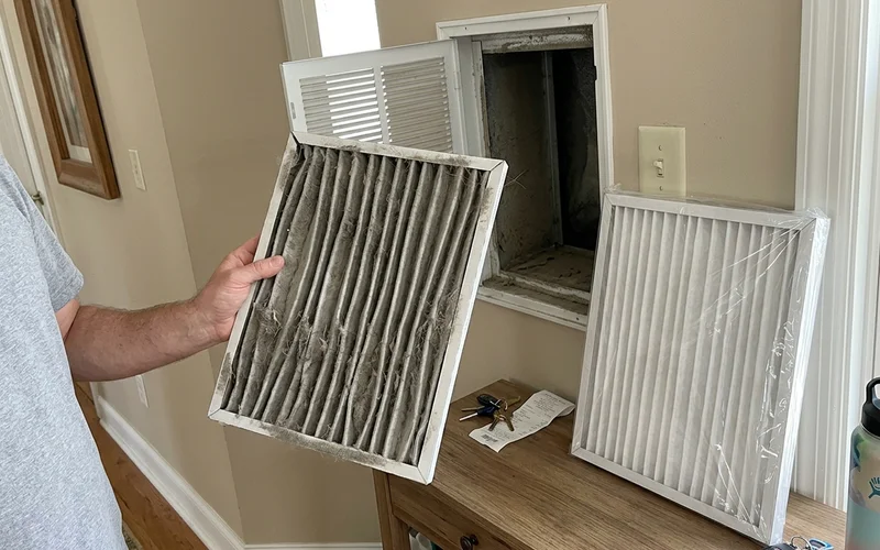 Dirty air filter pulled from a return grille held beside a new one
