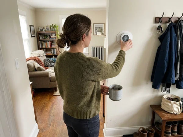 Person in a sweater adjusting a thermostat set to heat